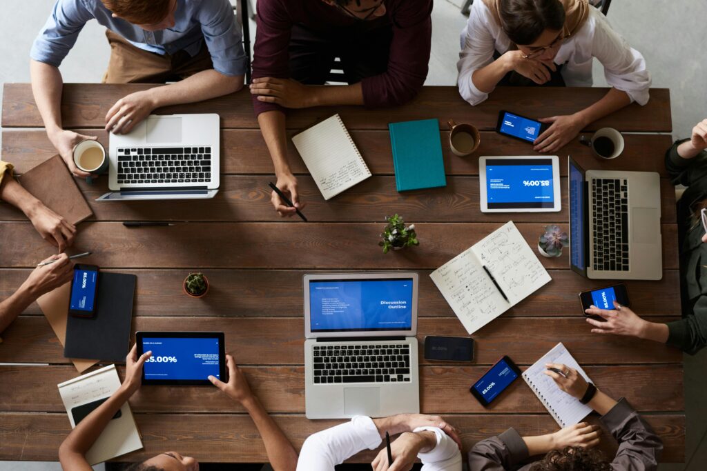 Overhead view of a diverse group of individuals working together at a wooden table with laptops, tablets, and notebooks, illustrating the concept of collaboration in a modern office setting.